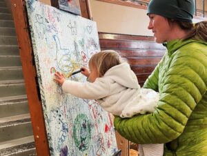 mother holds toddler painting on a canvas at the Laramie Plains Civic Center Artist Sunday event in Laramie, WY